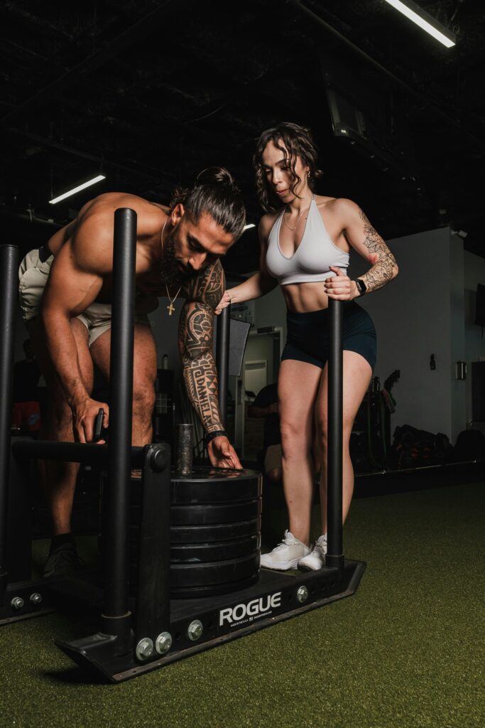 Two athletes working out together, using a sled push for fitness training indoors.